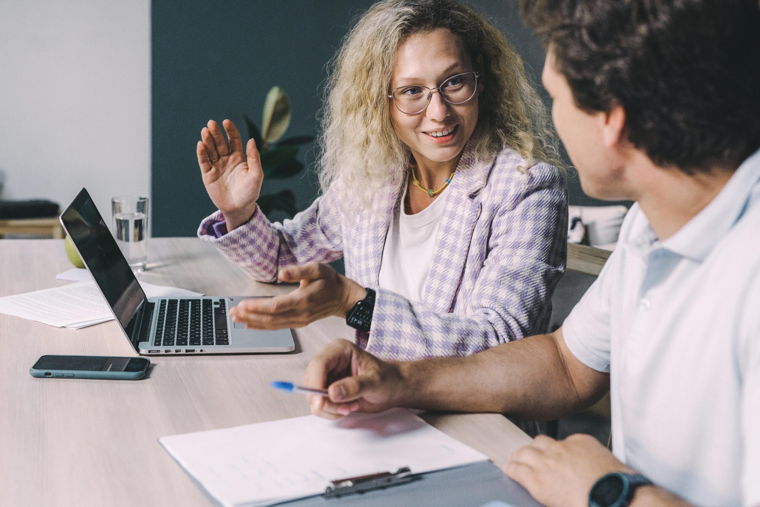 Two colleagues engaged in a lively discussion at an office desk, focusing on collaboration.